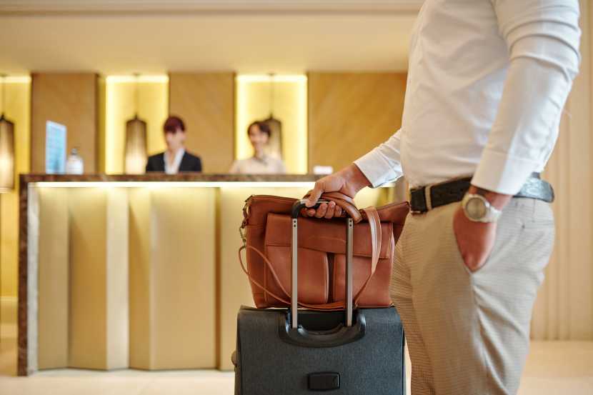 Cropped-image-hotel-guest-standing-lobby-with-luggage-after-checking - travel and tour world