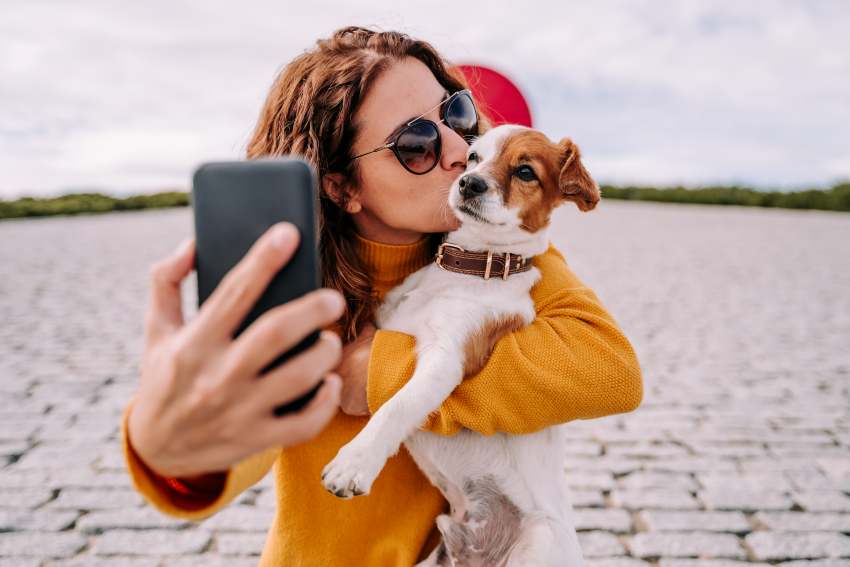 Smiling-woman-taking-selfie-while-standing-with-dog-outdoors - travel and tour world