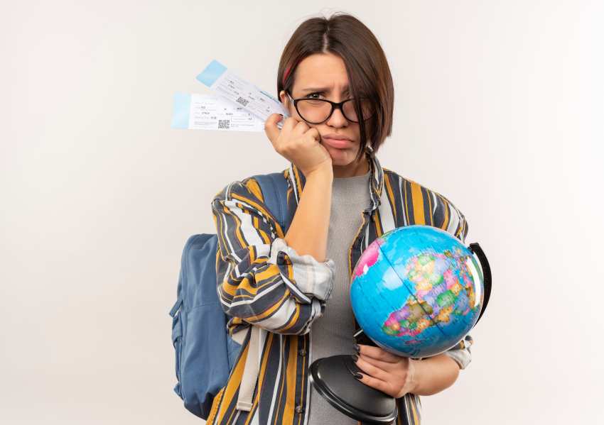 Unpleased-young-student-girl-wearing-glasses-back-bag-holding-airplane-tickets-globe-isolated-white-background-with-copy-space - travel and tour world