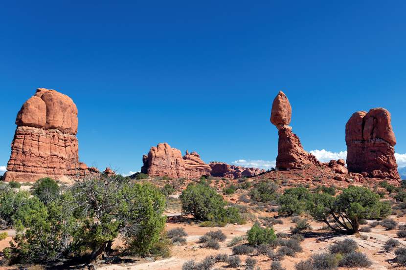 Scenic view of Arches National Park with iconic red rock formations and towering arches under clear skies, highlighting the stunning natural beauty of Utah’s desert landscape.