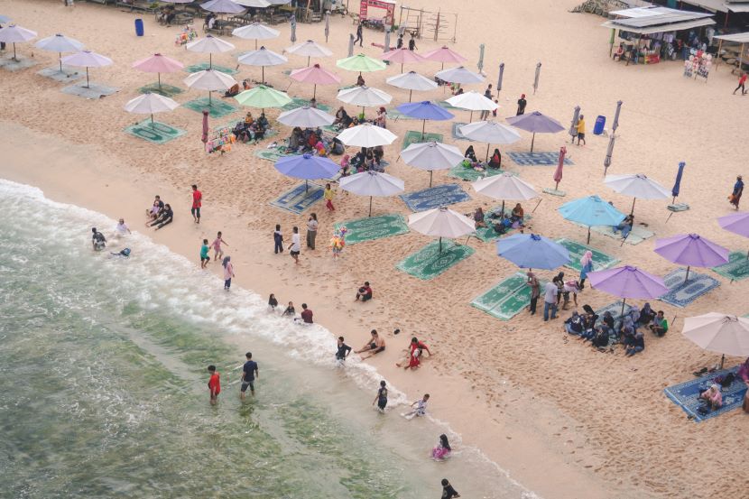 Ourists at pattaya beach navigating through rows of umbrellas and beach chairs, highlighting the ongoing debate over overcrowded beachfronts and their impact on tourism.