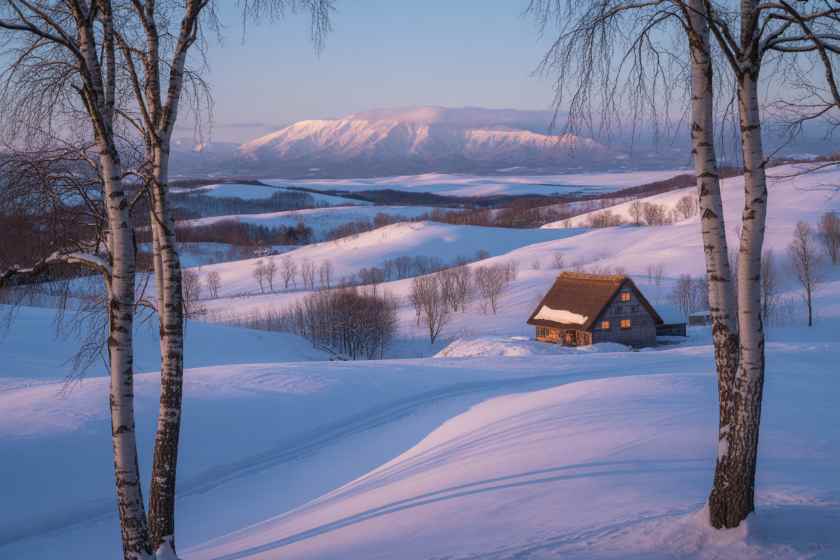 Beautiful snowy landscape in hokkaido with a cozy cabin and distant mountains.