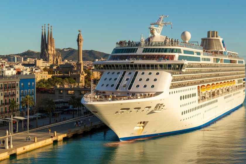 Luxury cruise ship docked at the port with barcelona skyline in the background.