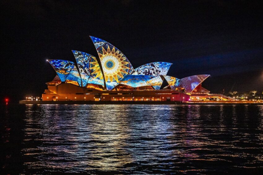 Sydney opera house with vibrant night light projections over water.