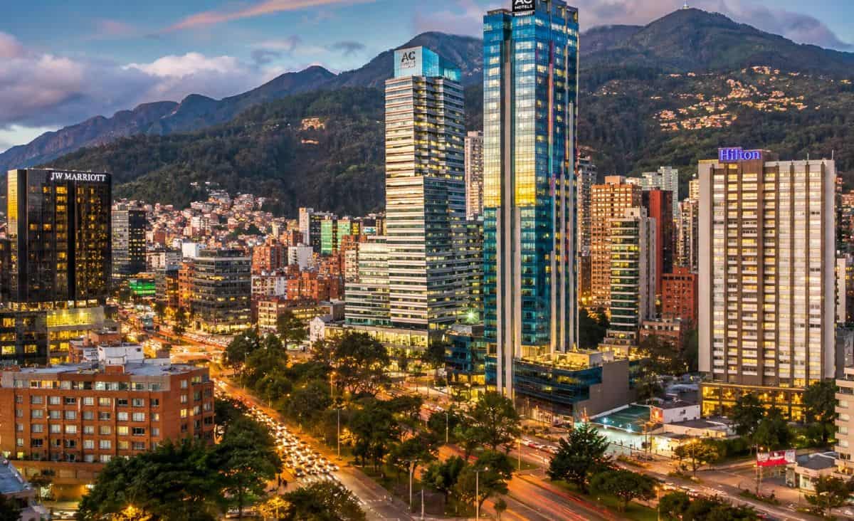 Bogotá skyline featuring modern hotels, vibrant city lights, urban architecture, and majestic andes mountains under a beautiful evening sky.