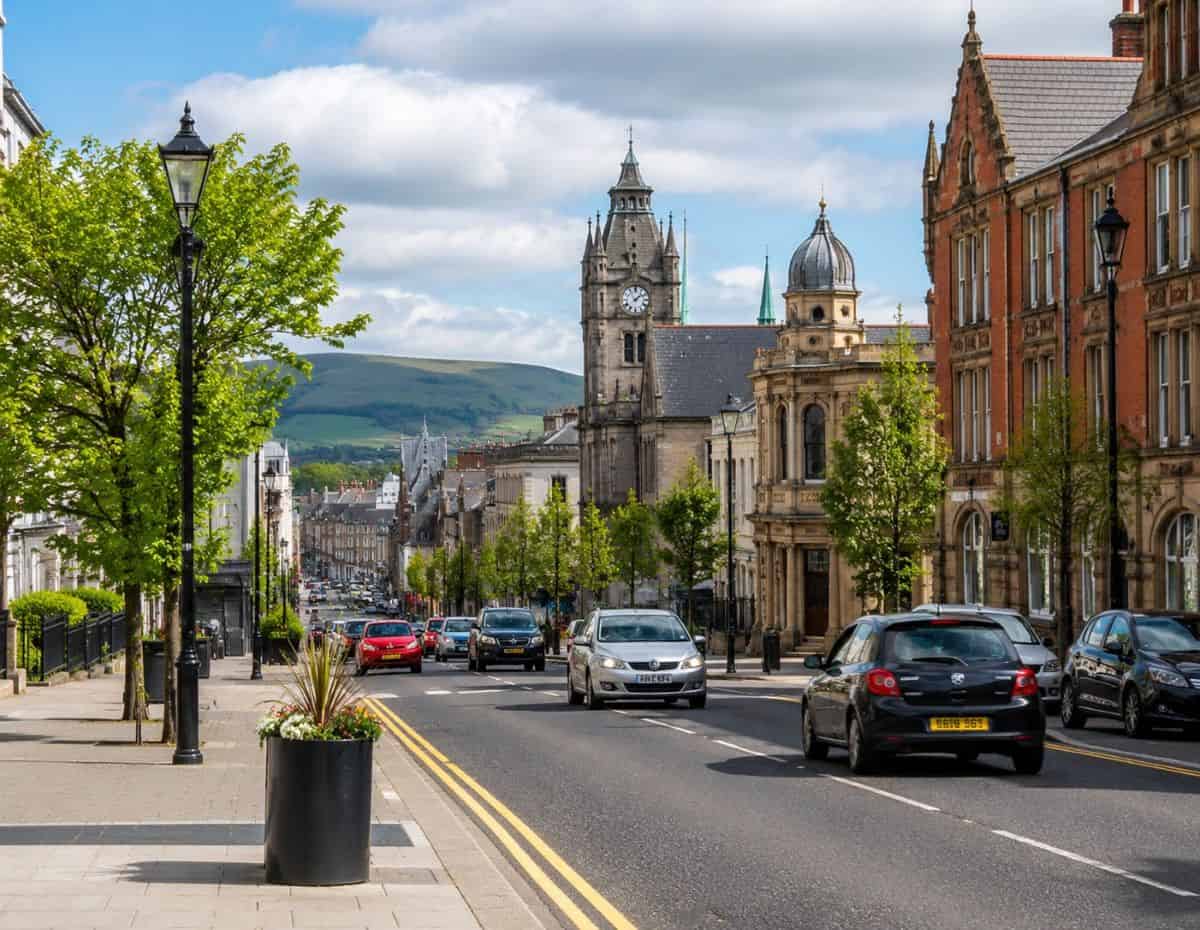 Ireland street with historic architecture, busy traffic, green hills, trees, and bright summer skies.