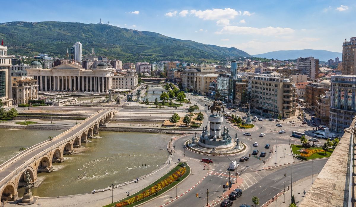 Macedonian cityscape featuring historic architecture busy roads scenic riverfront and stunning mountain views under clear skies - travel and tour world Macedonian cityscape featuring historic architecture, busy roads, scenic riverfront, and stunning mountain views under clear skies.