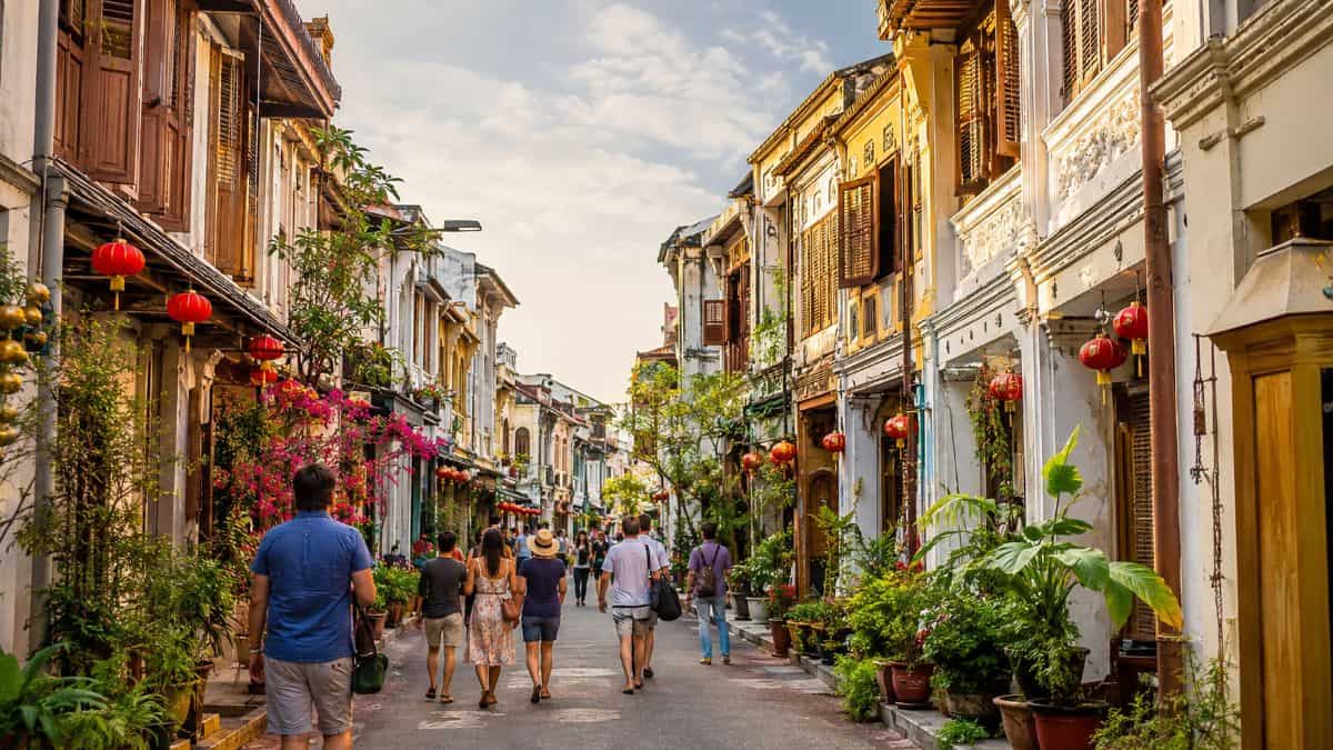 Tourists walking through a colourful historic southeast asian shophouse street lined with traditional architecture and local businesses.