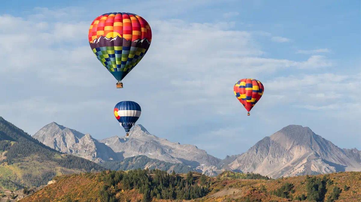 Colorful hot air balloon glowing and launching against the backdrop of the colorado rockies during peak autumn foliage at snowmass town park.