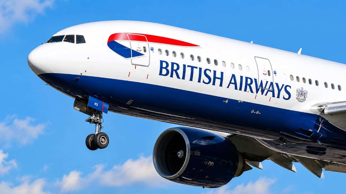 British airways passenger aircraft flying through a bright blue sky with landing gear extended and a large jet engine visible.