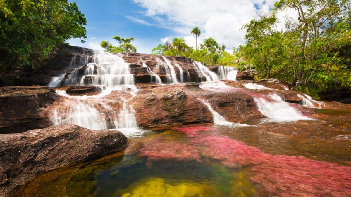 A scenic waterfall cascading over reddish-pink rock formations and lush green trees under a blue sky in colombia.