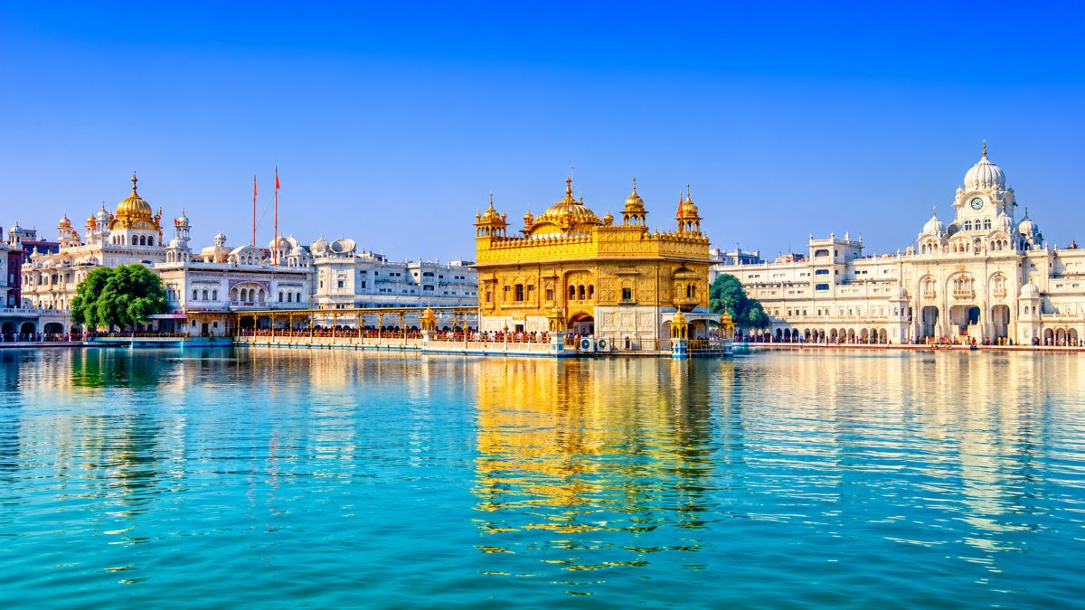 Golden temple in amritsar surrounded by white marble architecture, reflected in the turquoise waters of the amrit sarovar under a bright blue sky.