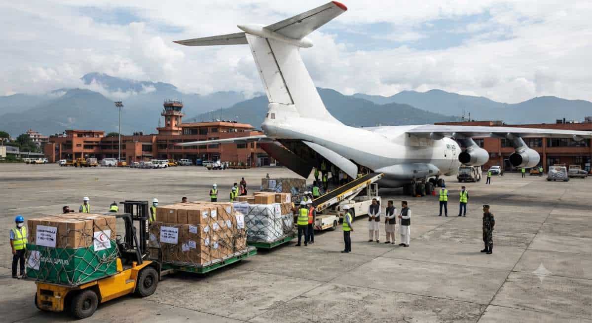 A cargo aircraft being loaded with humanitarian relief boxes and medical supplies at an airport tarmac to support flood victims in nepal.