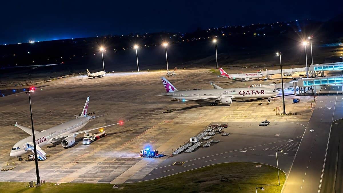 Night view of an international airport terminal with aircraft parked on the runway apron and airport lights illuminating operations.