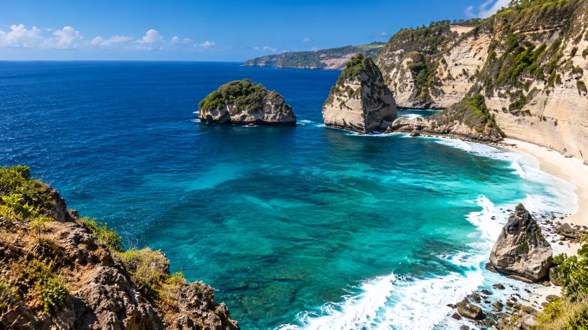 Ultra-realistic coastal landscape featuring turquoise waters, rugged limestone cliffs, green-covered sea stacks, white sandy shores and waves along a scenic tropical coastline