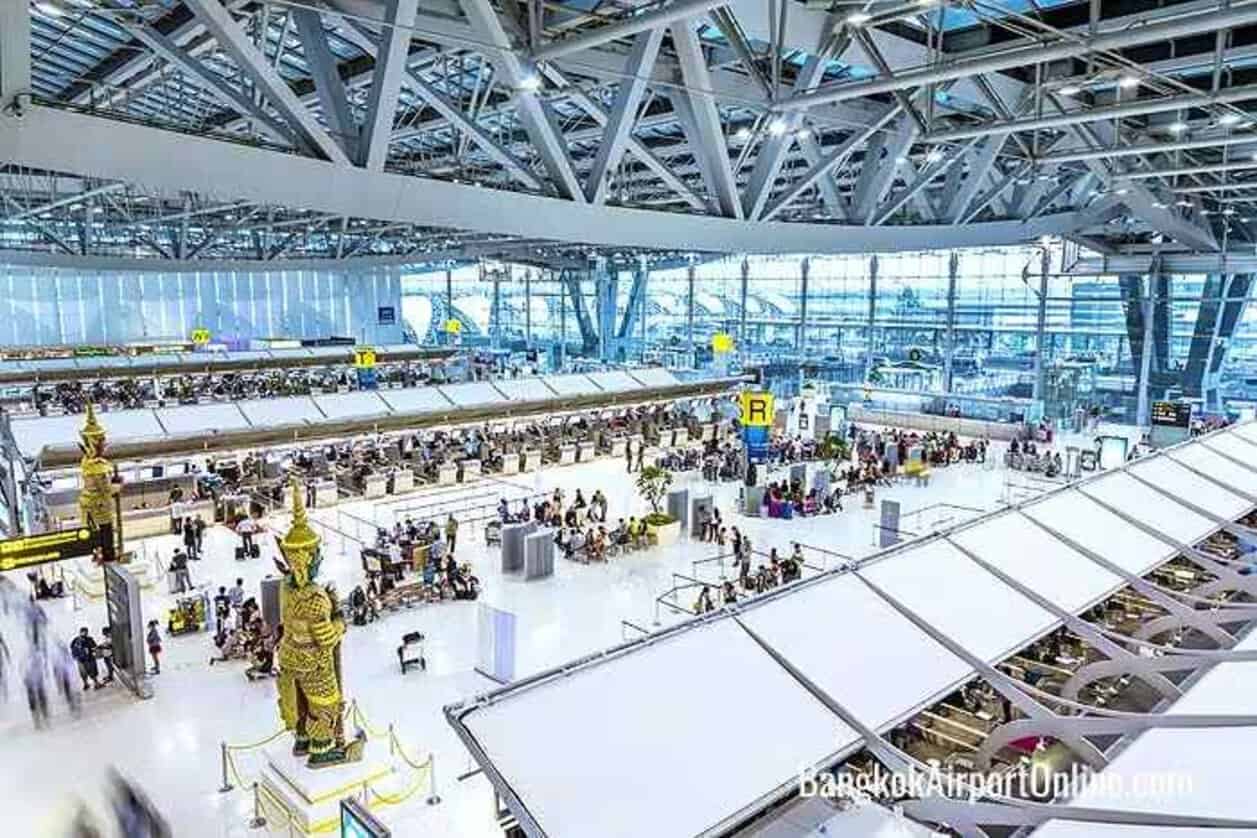 Suvarnabhumi airport terminal in bangkok with passengers queuing near check-in counters beneath its steel-and-glass roof.