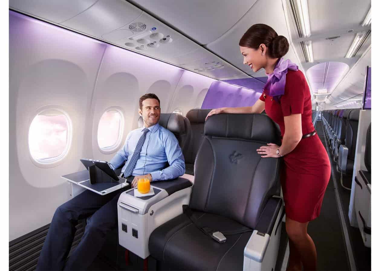 Virgin australia cabin crew member assisting a business-class passenger aboard an aircraft.