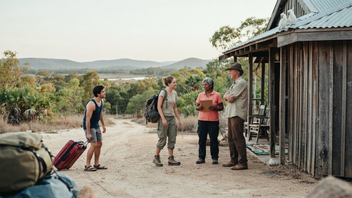 A farmer carries fresh produce through a sumba resort garden as guests dine outdoors.