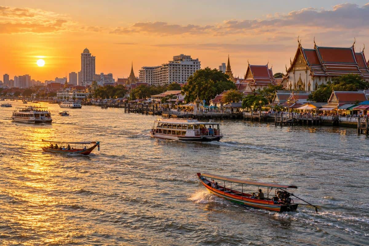 Thailand tourism is now finding new hope as domestic tourism revenue growth helps to offset the overseas decline - travel and tour world Long-tail boats and ferries on bangkok’s chao phraya river at golden hour, with riverside temples, hotels and markets.