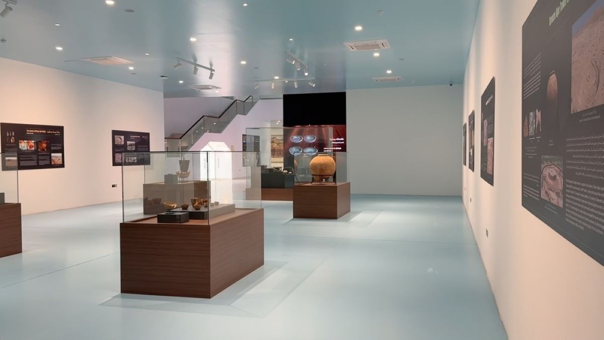 Bisya and salut - travel and tour world Interior view of the bisya and salut archaeological site visitor centre exhibition hall, featuring display cases with ancient artefacts, informative wall panels, and a sleek modern interior design with a pale blue ceiling.