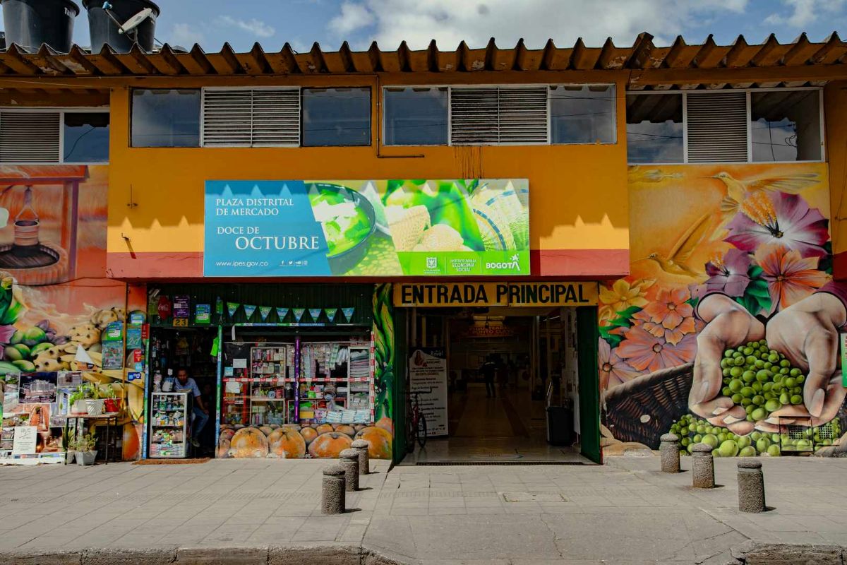 Colombia - travel and tour world Main entrance to the plaza distrital de mercado doce de octubre in bogotá, flanked by colourful painted murals and local shopfronts.