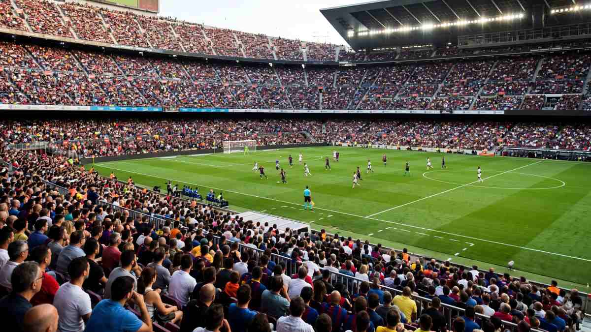 Europe sports tourism - travel and tour world Elevated wide shot of a packed european stadium with thousands of spectators watching an active football match on a lush green pitch.