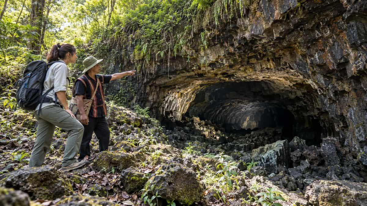 Exploring dak nongs basalt lava cave - travel and tour world A local guide points out a basalt lava cave to a traveller in vietnam’s dak nong geopark.