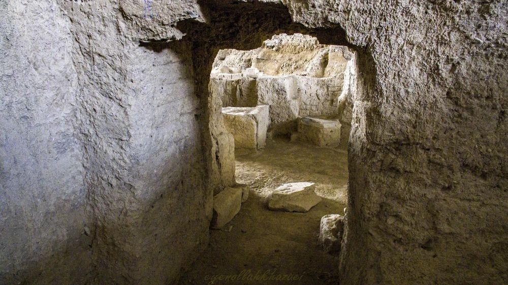 Hamadan - travel and tour world View through an ancient rough-stone doorway leading into excavated subterranean stone chambers at the hegmataneh archaeological site in hamadan, iran.