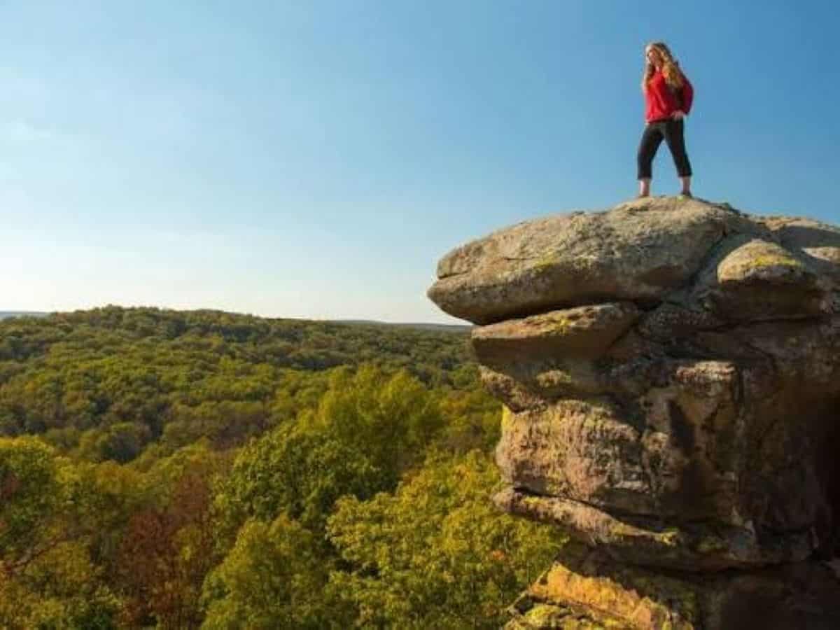 Illinois - travel and tour world Hiker standing on a rocky cliff overlooking an autumn forest.