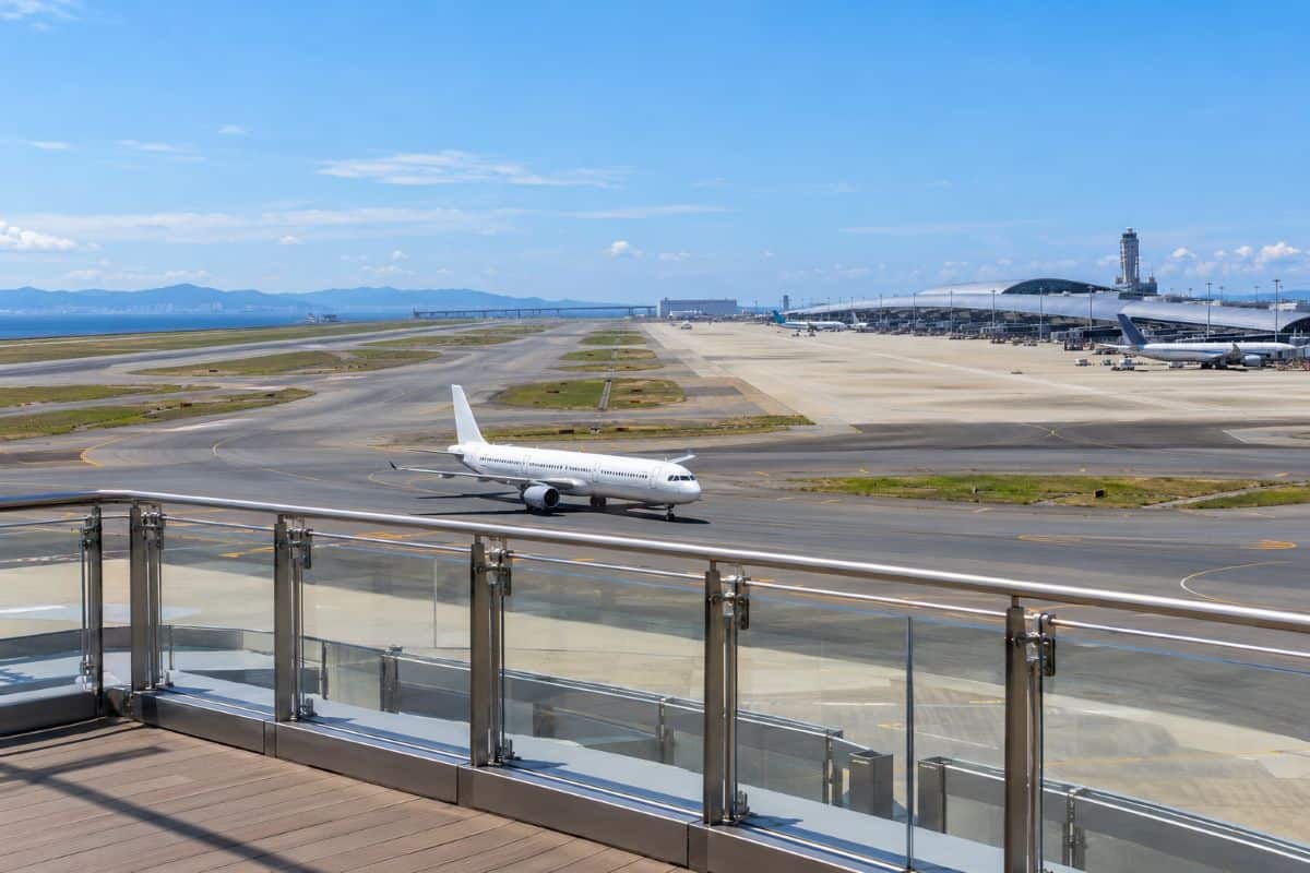 Passenger aircraft taxiing at kansai airport, viewed from an observation deck with the terminal and sea beyond.