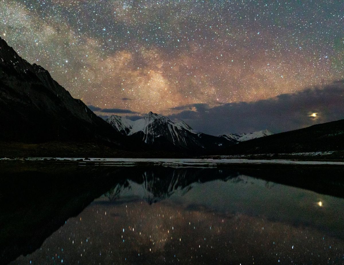 Jasper national park - travel and tour world A night sky filled with stars and the milky way stretching over snow-capped mountains and reflecting in a still lake.