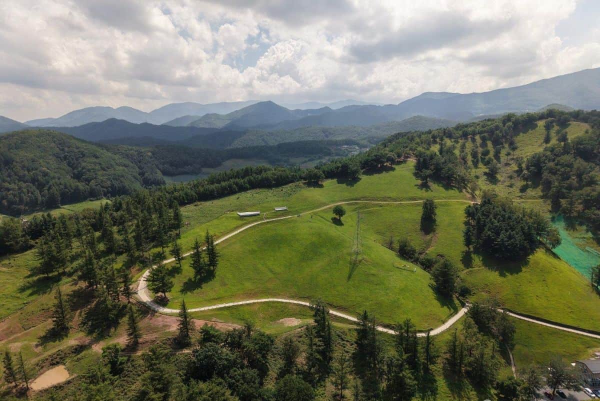 Aerial view of lush green mountain landscapes, winding paths and forested hills under a cloudy sky