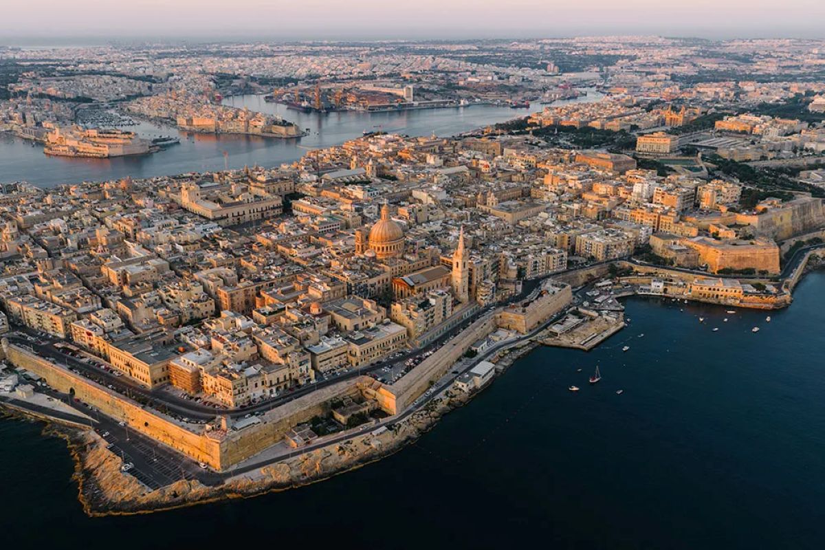 Aerial view of valletta, malta, with limestone buildings, a domed church and waterfront fortifications in warm evening light