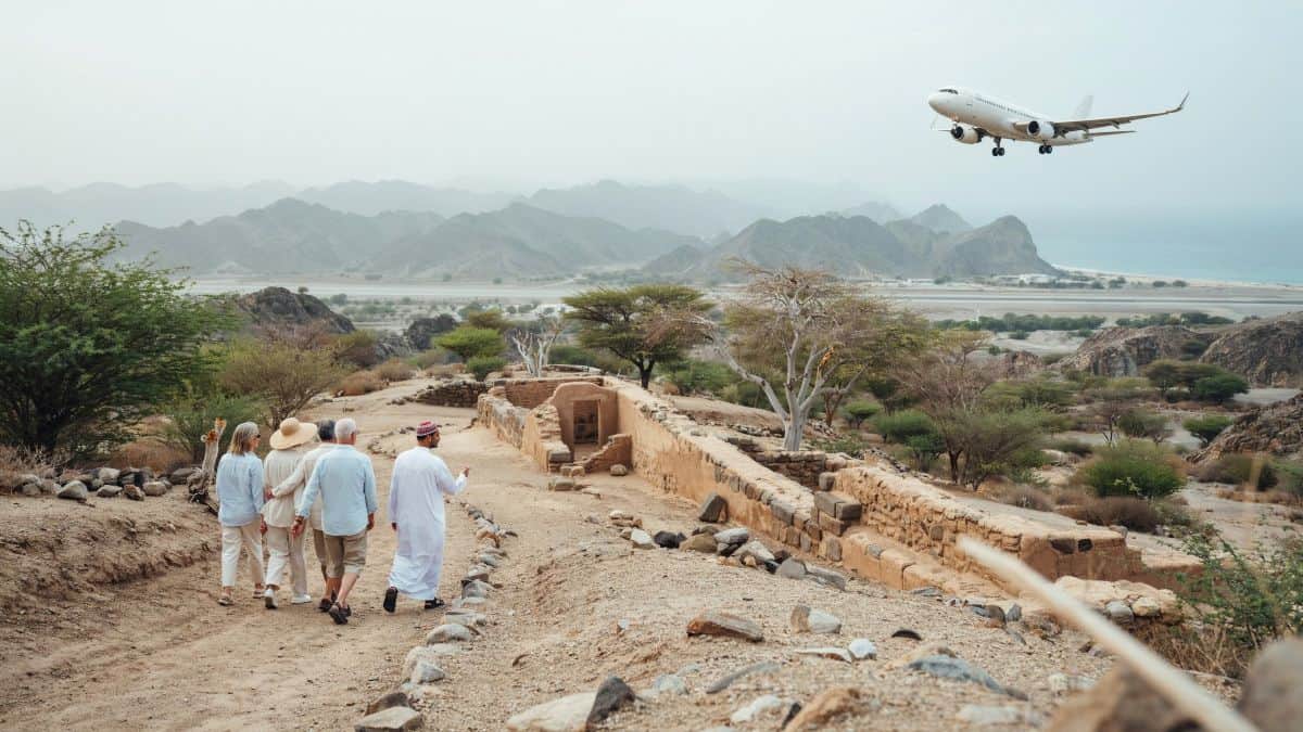 Oman air routes - travel and tour world Visitors explore a dhofar heritage site with a local guide as an aircraft approaches salalah airport, highlighting oman’s expanding tourism links.