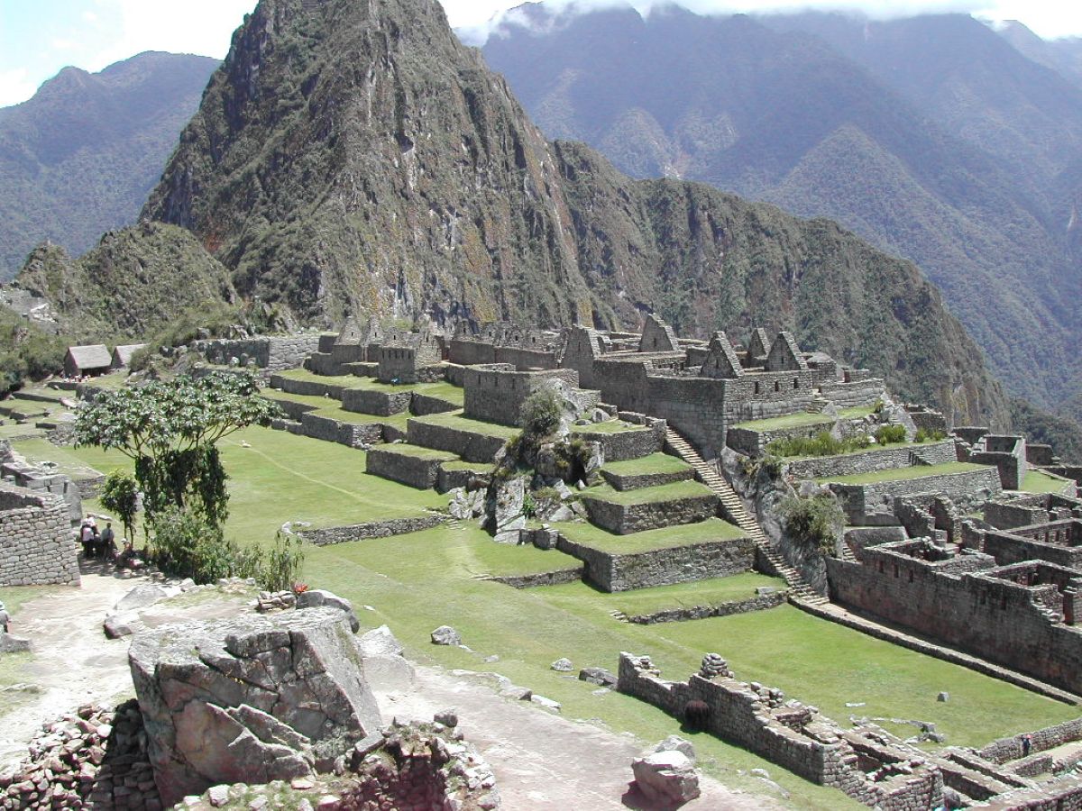 Panoramic view of the ancient inca ruins of machu picchu in peru, featuring stone structures and terraced green fields set against steep mountain peaks.