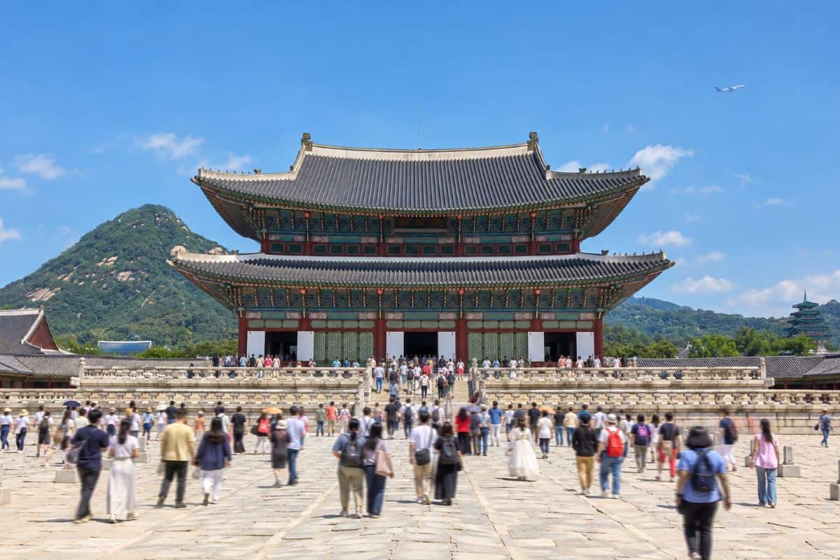 South korea is seeing the growth of seoul tourism as more visitors and card spending now unlock new opportunities - travel and tour world Visitors in the courtyard of gyeongbokgung palace in seoul, south korea, with green mountains behind.