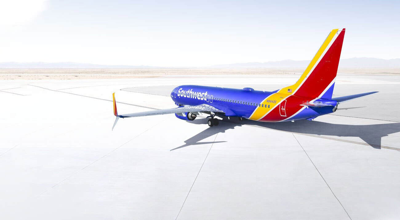 Southwest airlines carry-on suitcase at a tsa ct security scanner in a us airport, with a branded southwest aircraft in the background.