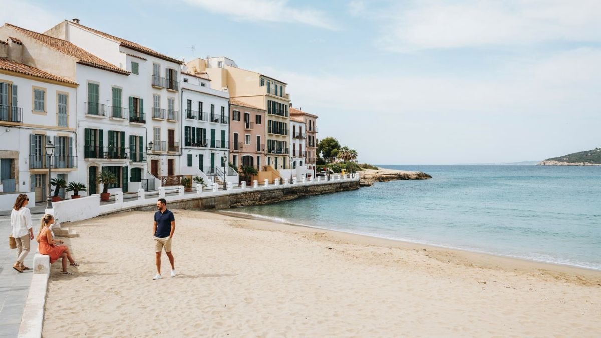 Spain is seeing more hotel nights as hotel prices climb 67 and put new pressure on travel budgets - travel and tour world Pastel waterfront buildings overlook a sandy beach and calm turquoise bay, with visitors beside the promenade