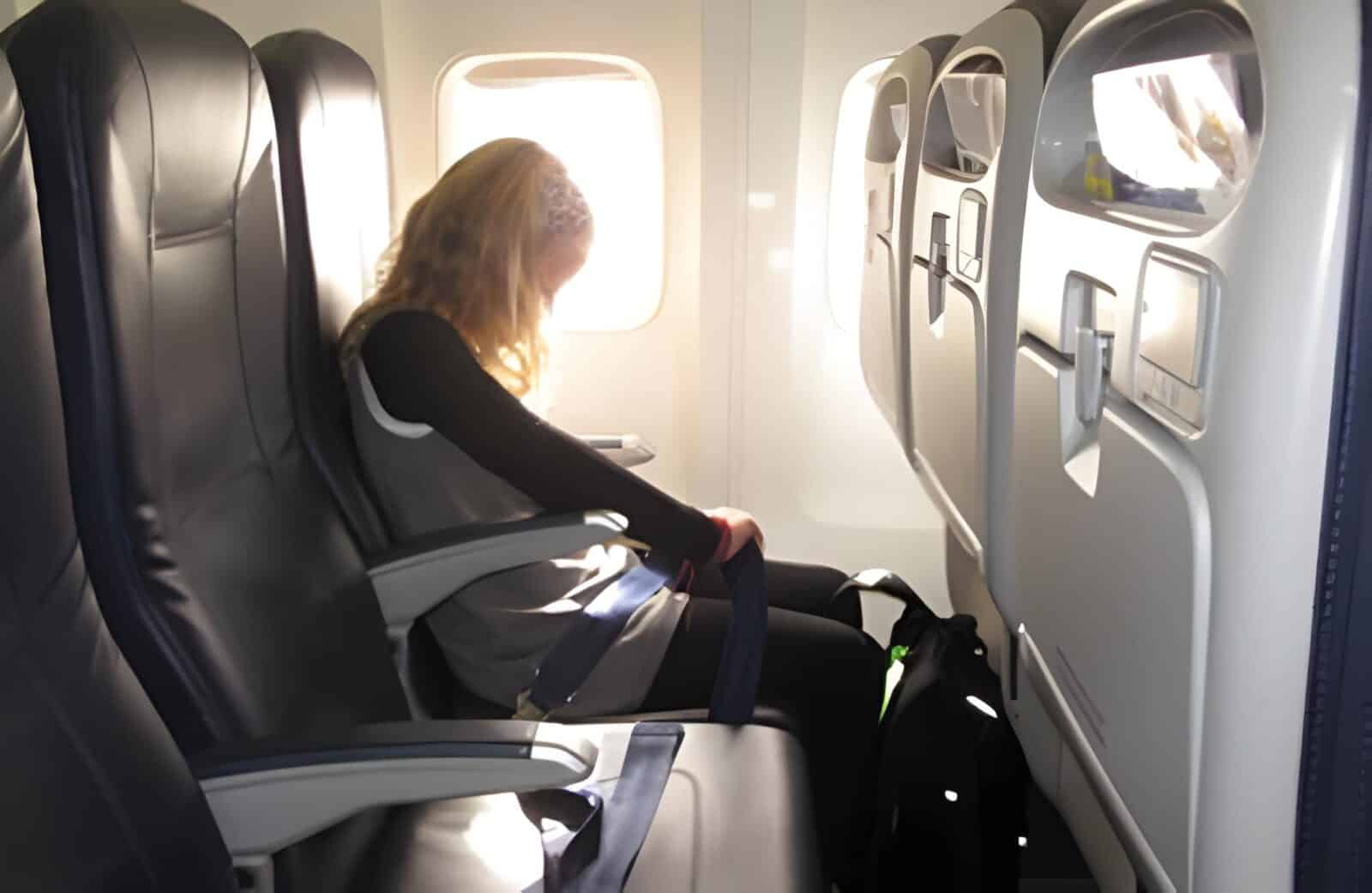 Uk travel - travel and tour world Passenger with long blonde hair seated beside an aircraft window, with empty black leather seats alongside.