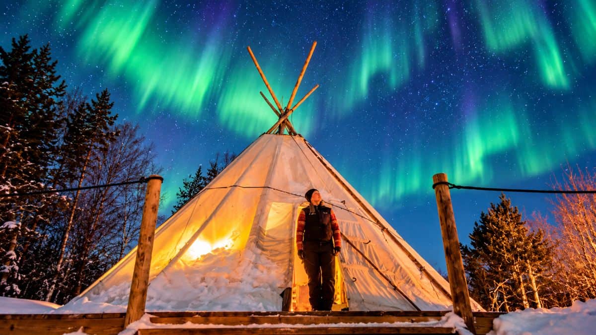 Ultra-realistic arctic tipi glowing beneath a vivid green aurora borealis surrounded by snowy trees and a star-filled night - travel and tour world Ultra-realistic arctic tipi glowing beneath a vivid green aurora borealis, surrounded by snowy trees and a star-filled night