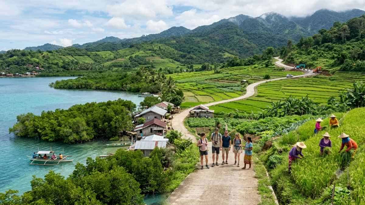 A realistic documentary-style photograph capturing an integrated agri-ecotourism corridor in rural asia, featuring tourists walking along a paved road alongside local farmers harvesting terraced rice fields, with protected coastal mangroves, a passenger boat in clear blue waters, and distant highland road construction against forested mountains.
