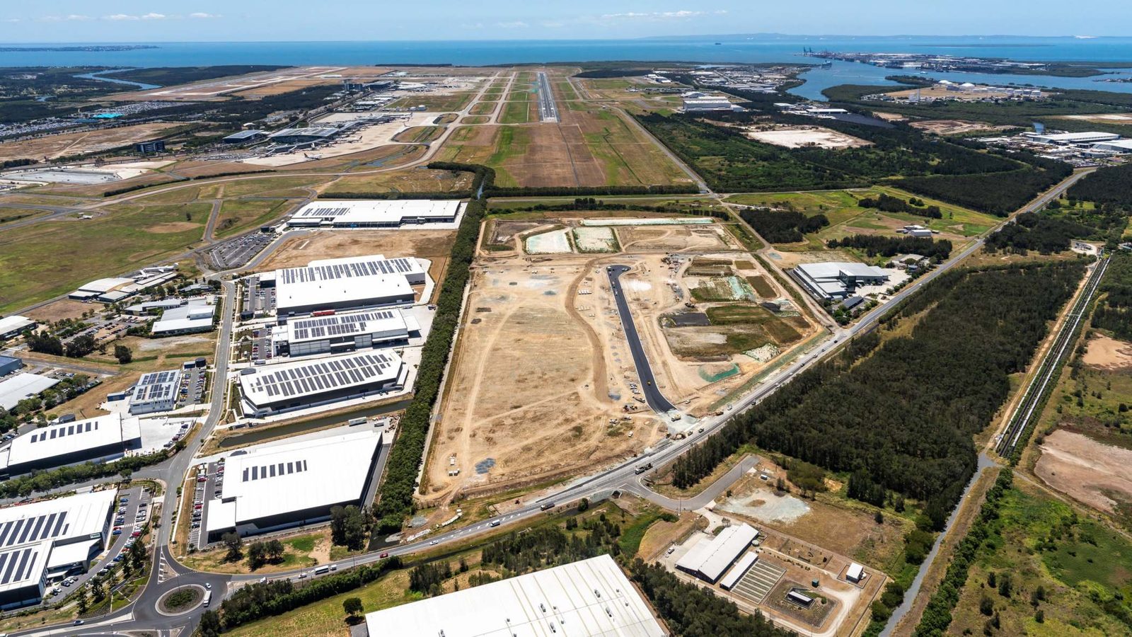 Brisbane-airport-industrial-land-release-logistics-expansion - travel and tour world Aerial view of brisbane airport industrial expansion, featuring logistics warehouses, development sites and runways.