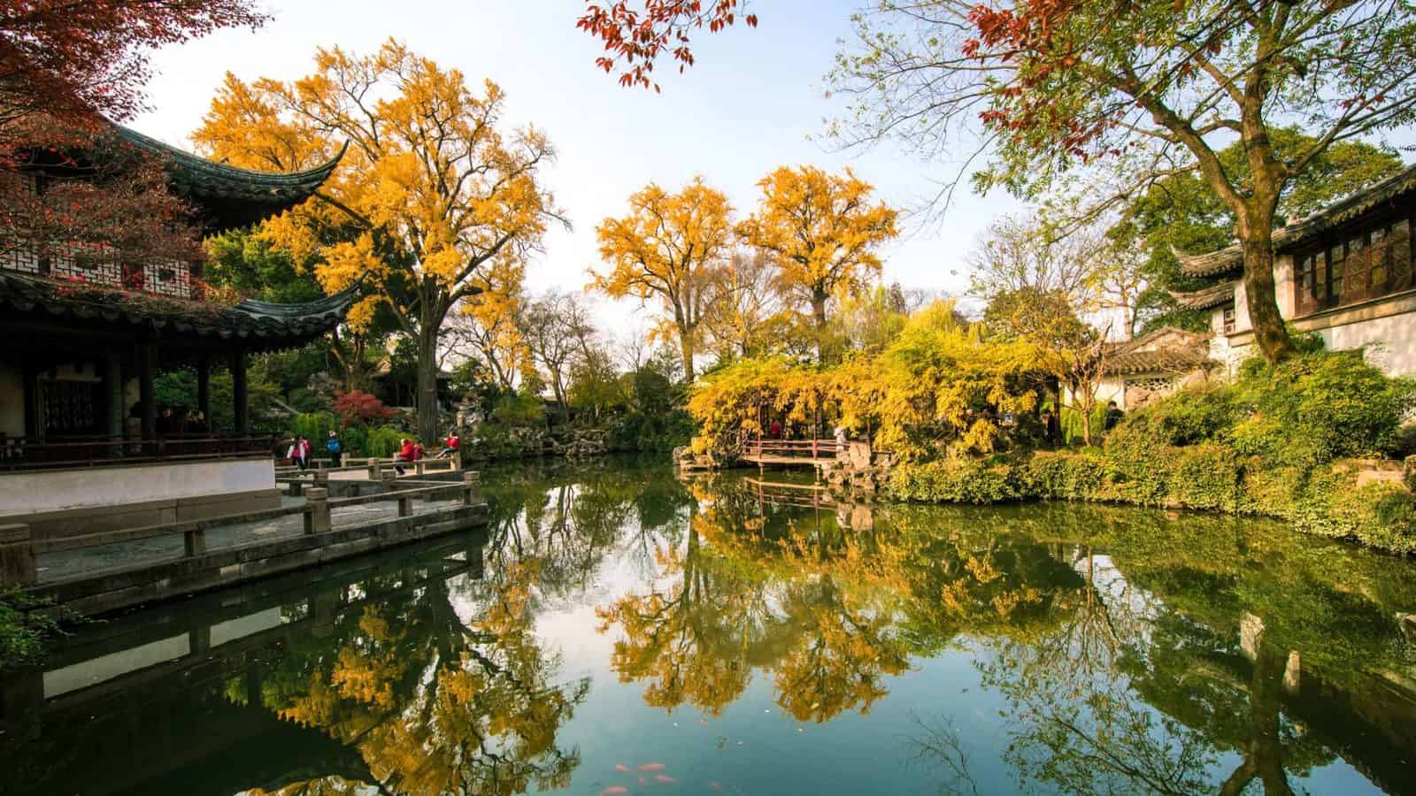 Traditional suzhou garden with golden autumn trees, chinese pavilions and peaceful pond reflections.