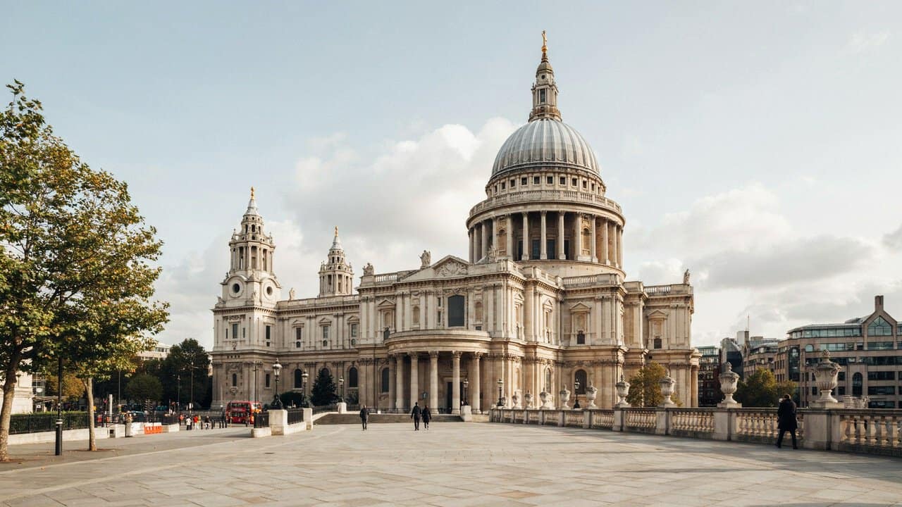 Cathedral restoration - travel and tour world St. Paul's Cathedral in London featuring its prominent dome and grand classical facade above a wide paved plaza with scattered pedestrians under a partly cloudy sky.