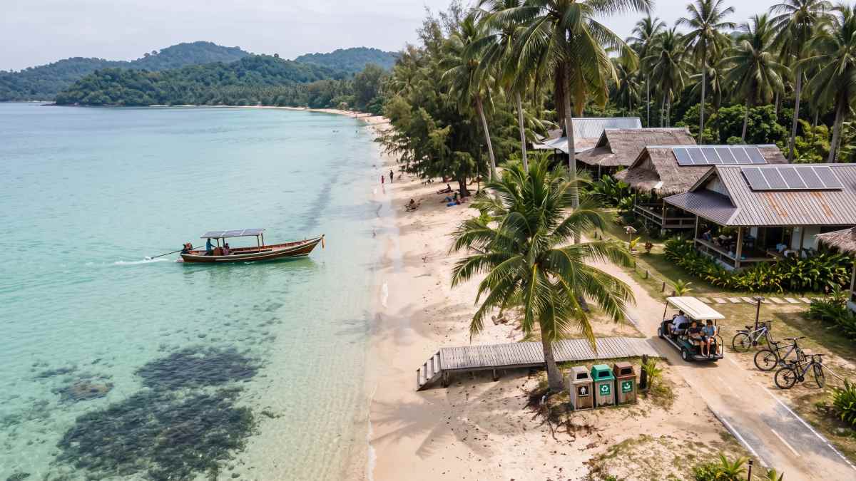 Islands tourism - travel and tour world An aerial travel photograph of a small, lush southeast asian island showing sustainable tourism with rooftop solar panels on eco-resorts, solar-powered electric boats, and community transport carts along a tranquil turquoise beach with visible coral reefs and few tourists.