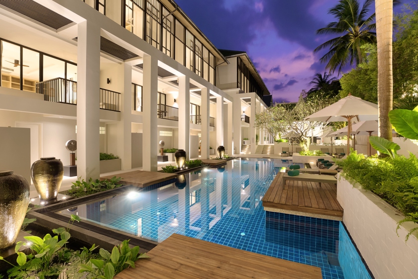 Outrigger-surin-beach-resort-luxury-swimming-pool-phuket-thailand - travel and tour world Illuminated swimming pool at outrigger surin beach resort in phuket, with tropical gardens and poolside loungers at dusk.