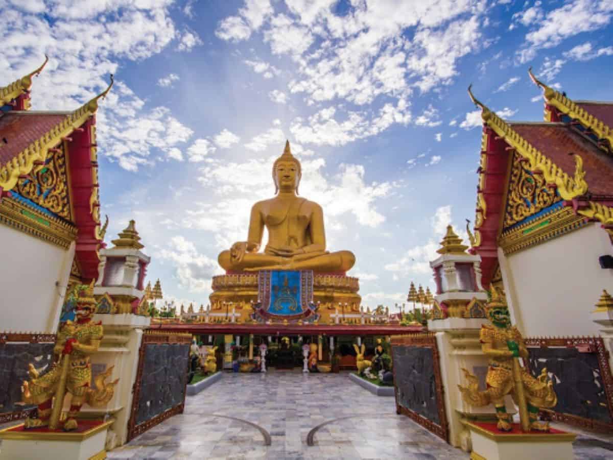 Thailand tourism - travel and tour world Large golden buddha statue seated at a traditional thai temple with guardian statues at the gates.