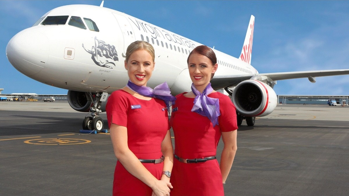 Virgin australia cabin crew stand in front of a passenger aircraft at an australian airport.